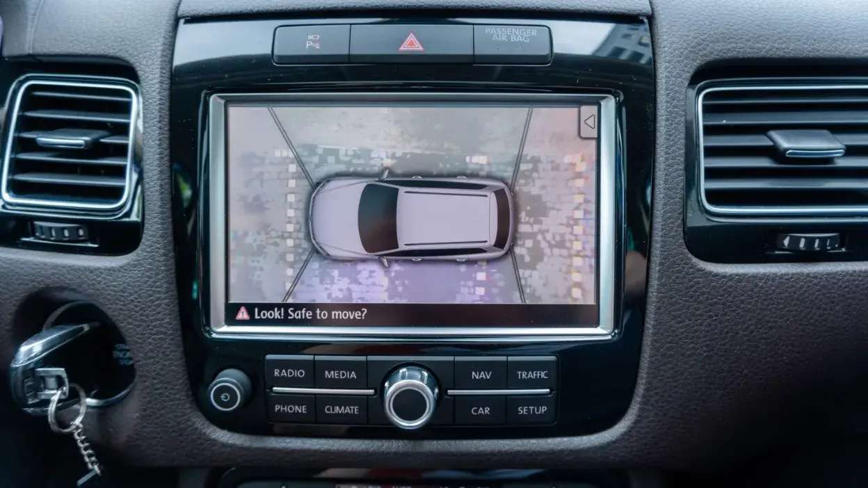 Ecrã de sistema de estacionamento com visão aérea do carro e aviso de segurança.