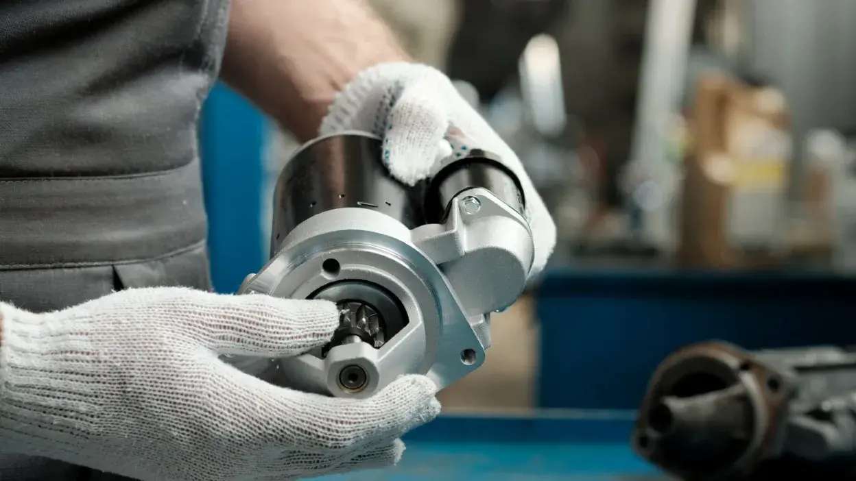 Pessoa com luvas a segurar um motor de arranque automóvel em oficina mecânica