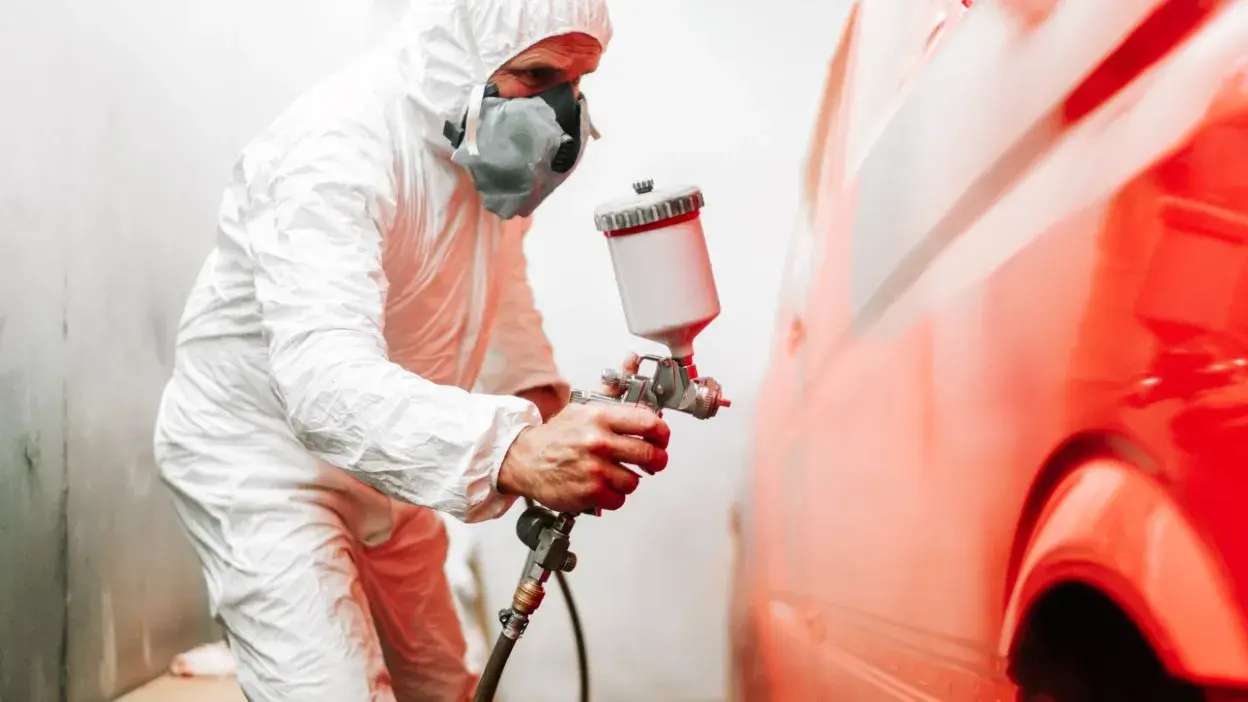 Pessoa com fato e máscara a pintar carro vermelho com pistola de pintura