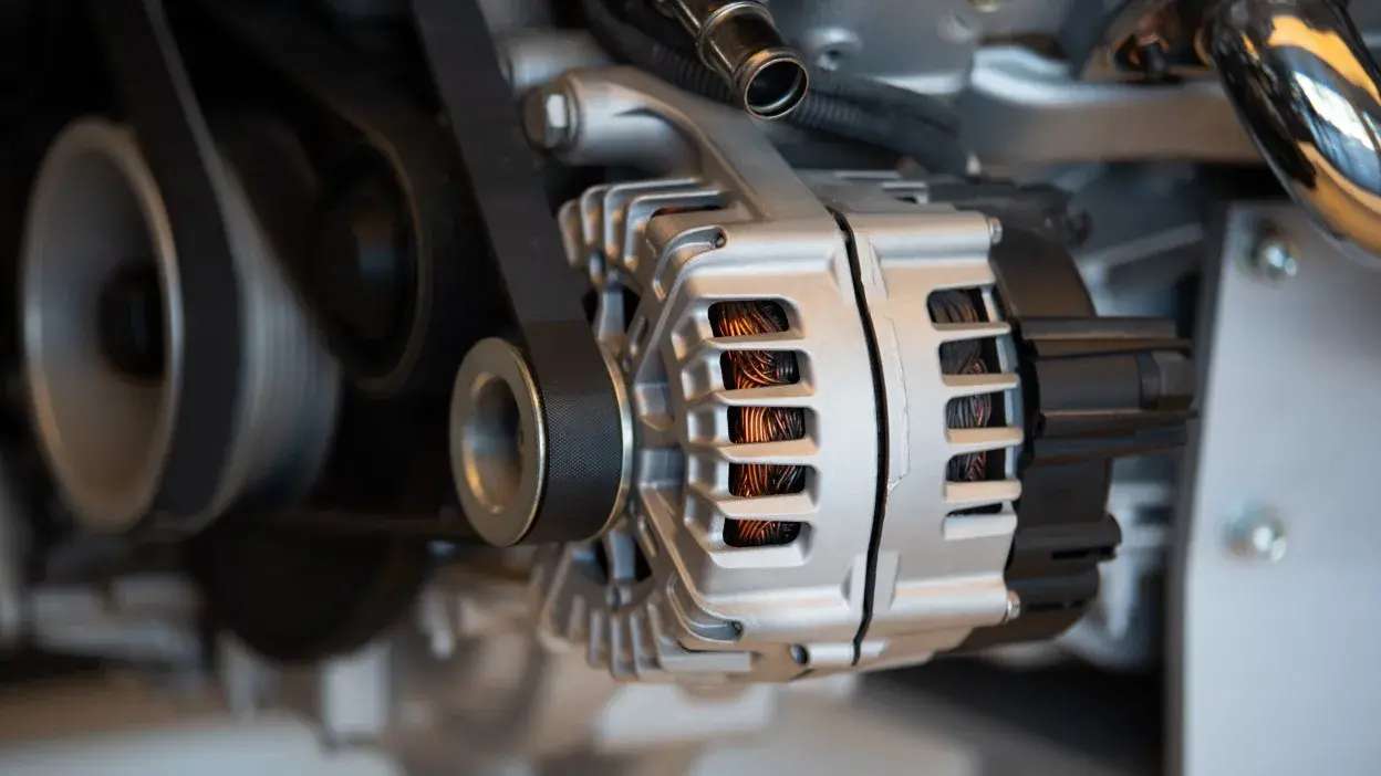 Alternador metálico ligado a correia num motor de automóvel.