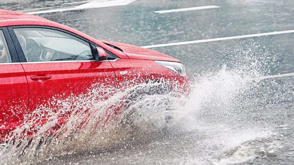 Carro vermelho a passar por poça de água com salpicos elevados na estrada molhada