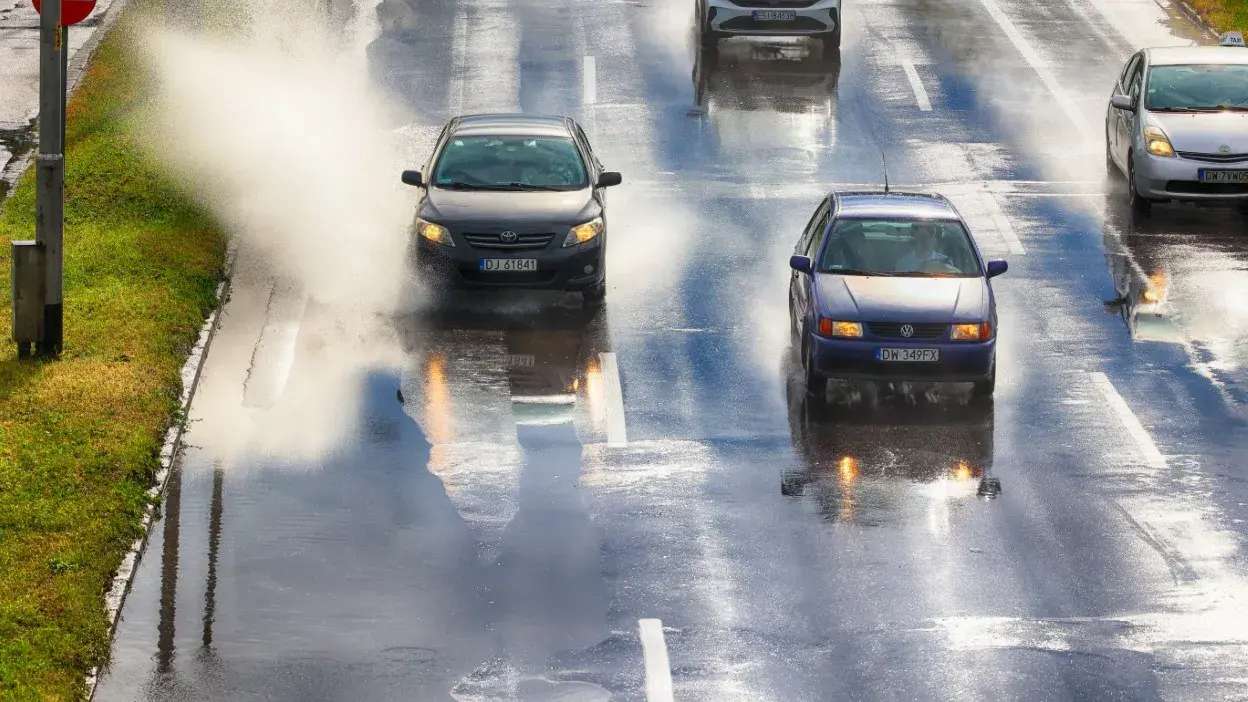Dois carros a passar por estrada molhada com água a salpicar nas laterais