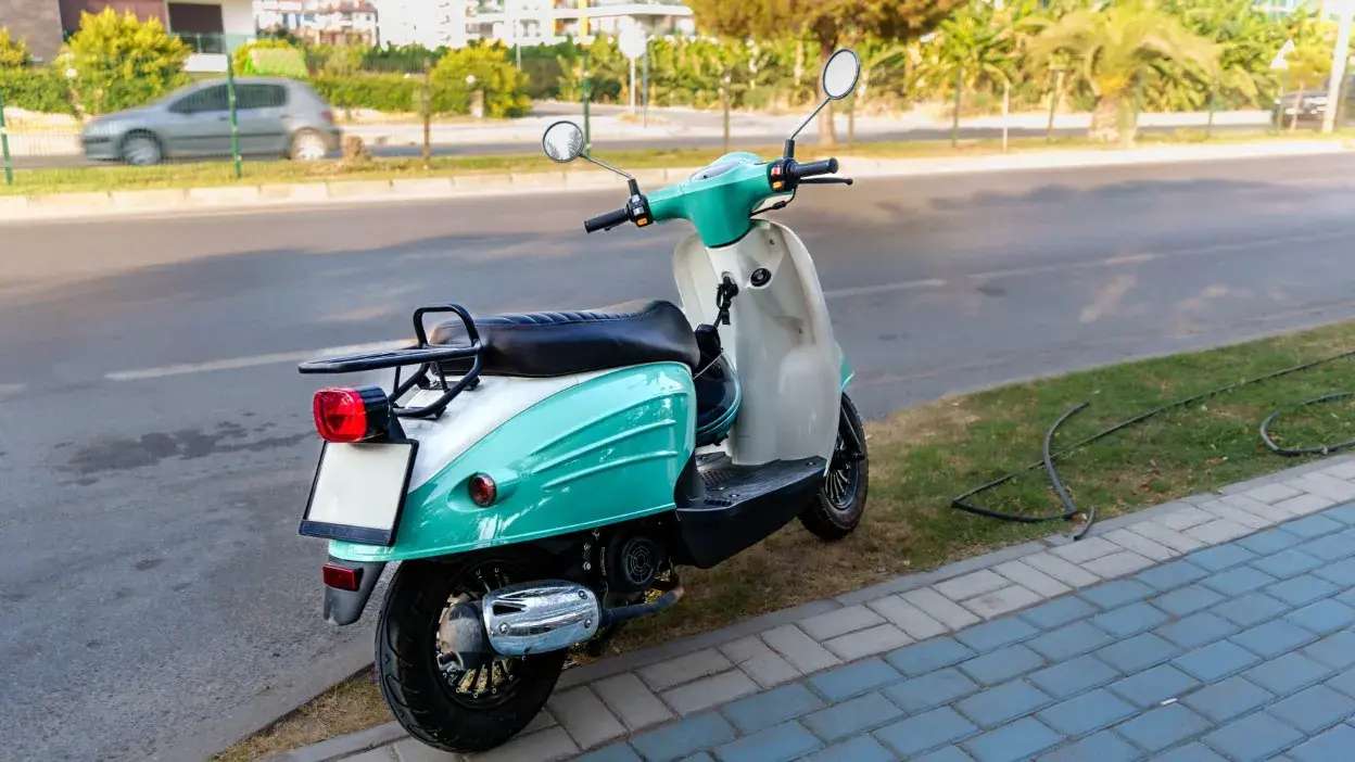 Ciclomotor verde e branco estacionado junto a passeio e estrada urbana