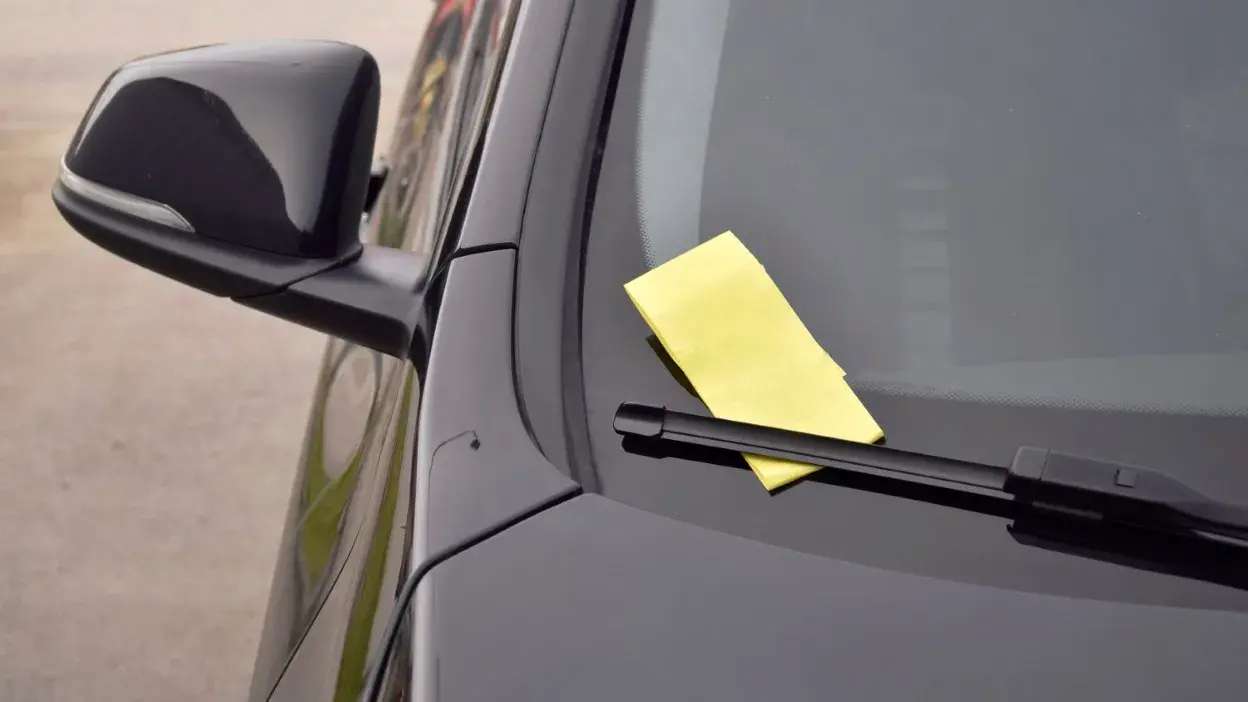 Nota amarela colocada sob o limpa para-brisas de um carro preto estacionado.