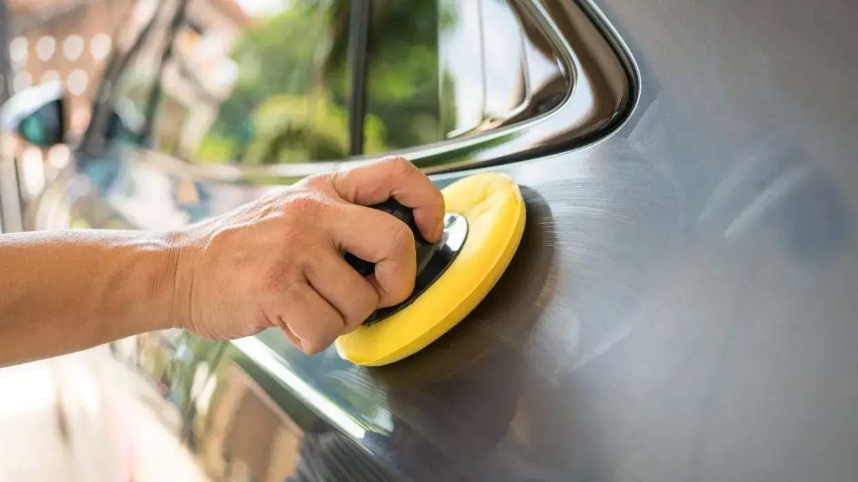 Mão a polir a porta de um carro com uma esponja amarela.