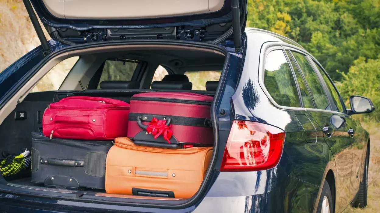 Mala vermelha, mala redonda e mala laranja no porta-bagagens de um carro azul aberto numa zona rural