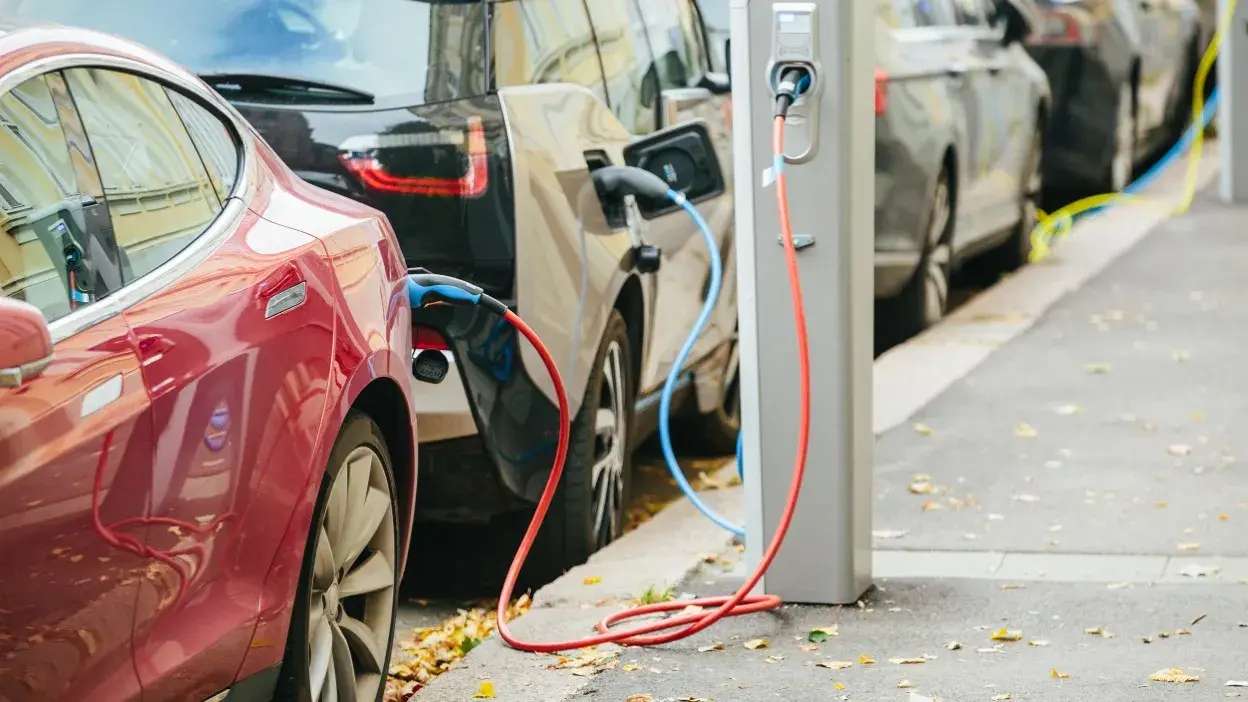 Vários carros elétricos estacionados numa rua a carregar em postos de carregamento público.