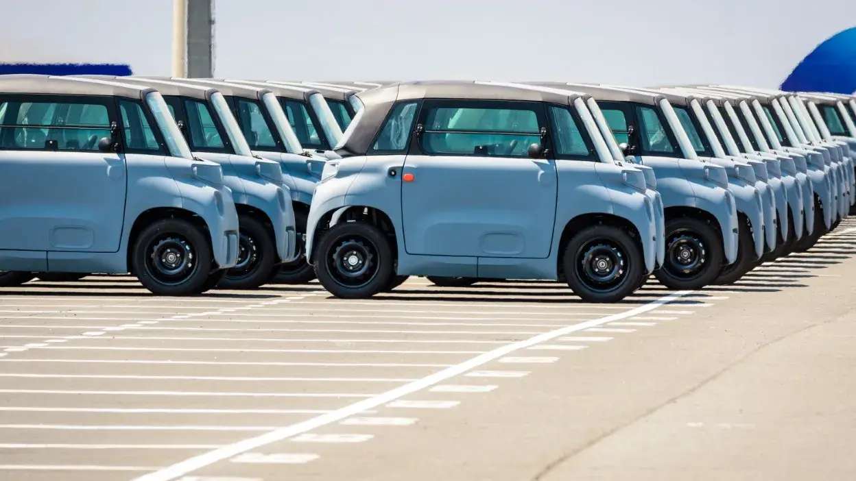 Vários microcarros azuis estacionados em fila num parque de estacionamento ao ar livre.