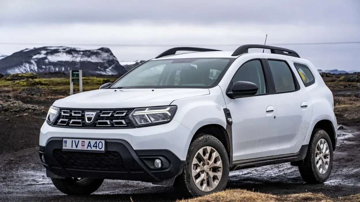 SUV Dacia Duster branco estacionado em terreno montanhoso com montanhas ao fundo.