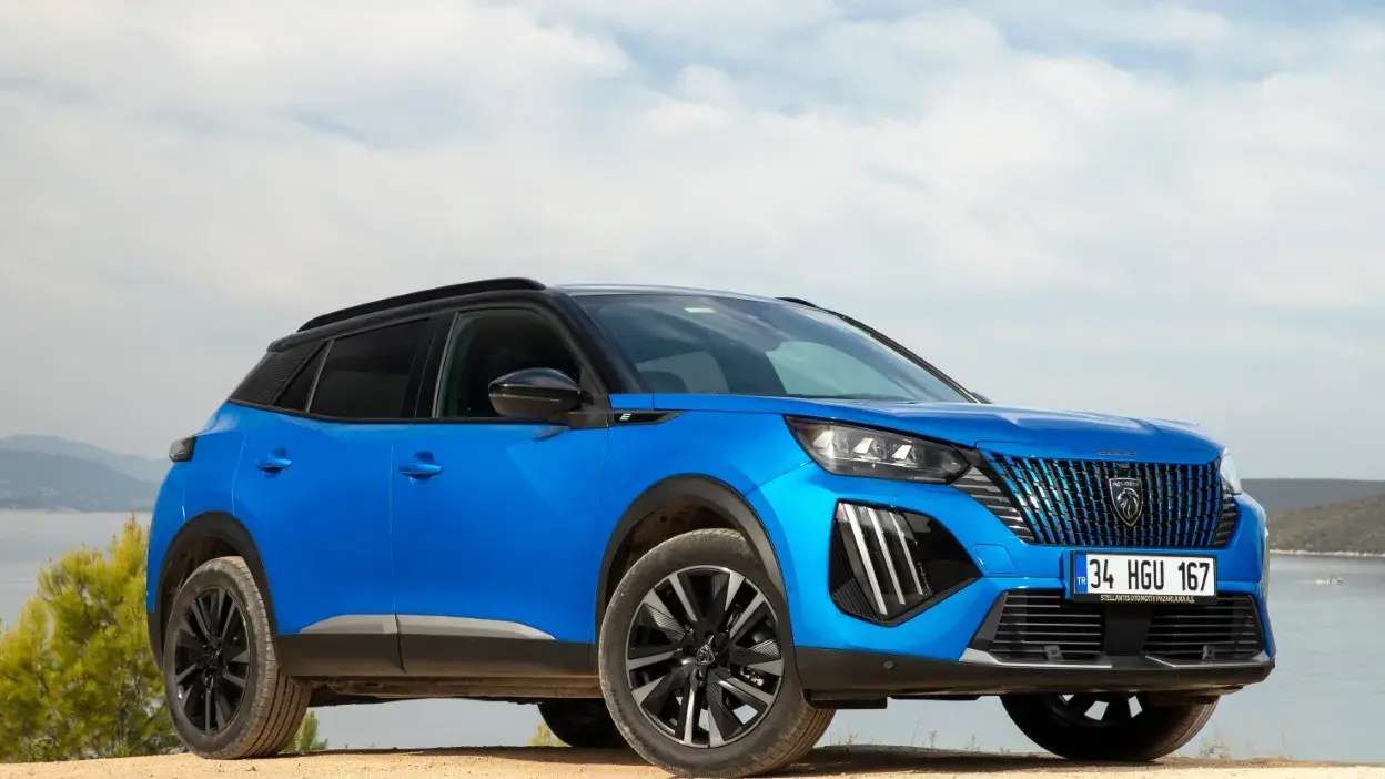 Carro Peugeot SUV azul estacionado em terreno arenoso com céu nublado ao fundo