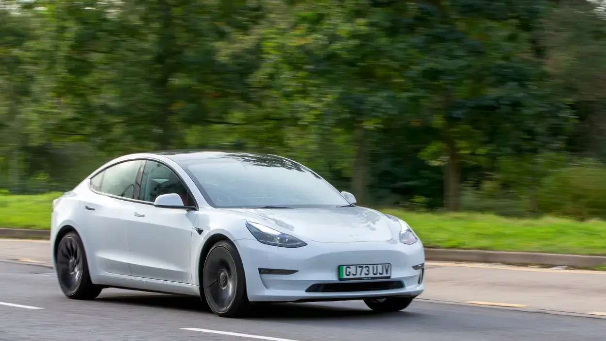 Carro elétrico branco em movimento numa estrada com árvores ao fundo