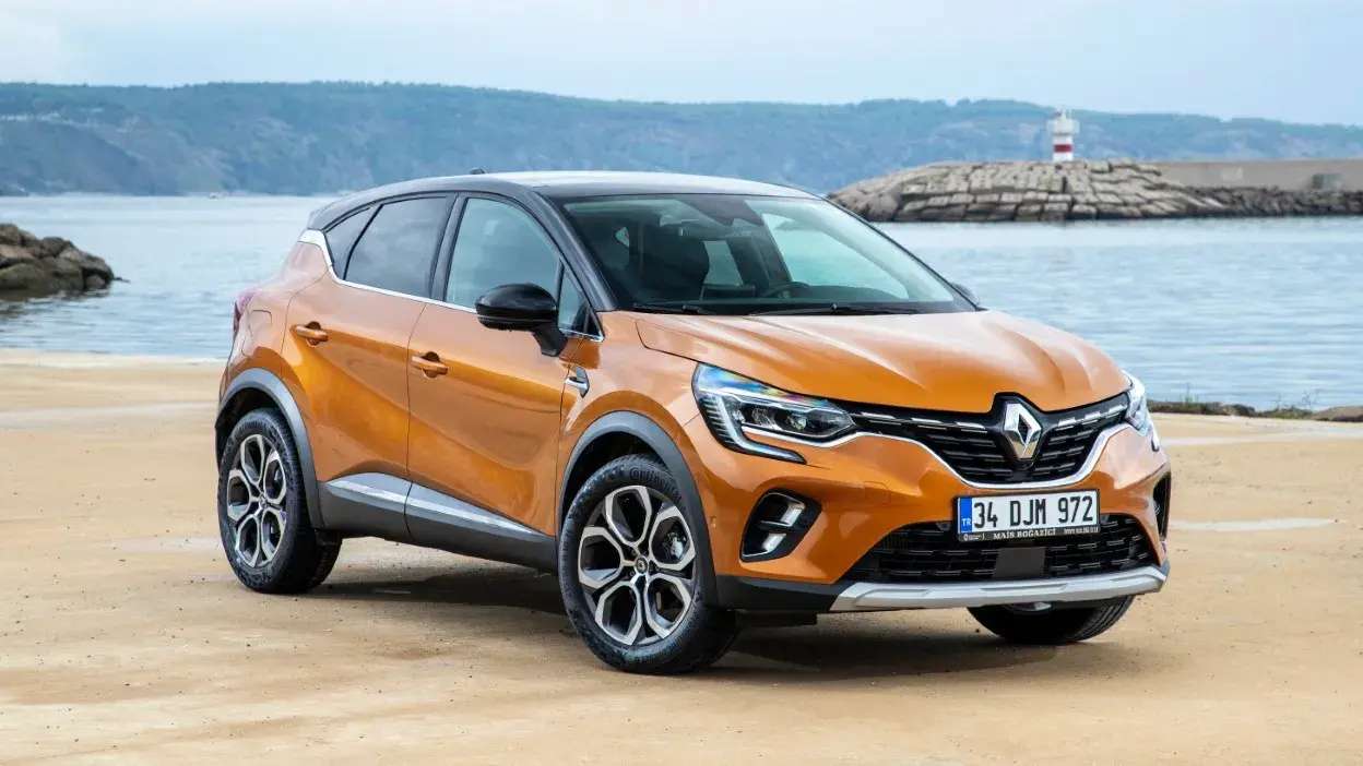 Carro Renault Captur laranja estacionado numa praia com mar e farol ao fundo