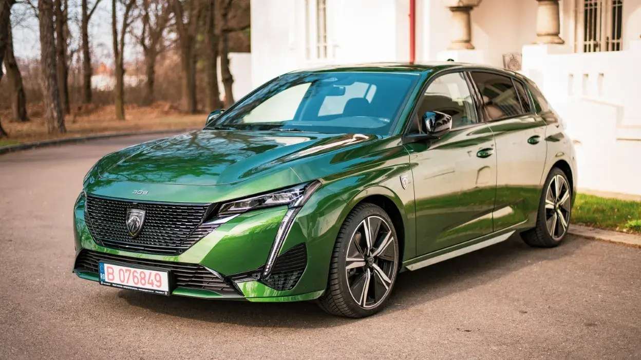 Carro Peugeot 308 verde estacionado junto a um passeio com árvores ao fundo