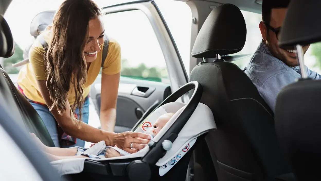 Mulher a colocar bebé em cadeirinha Isofix no banco traseiro do carro