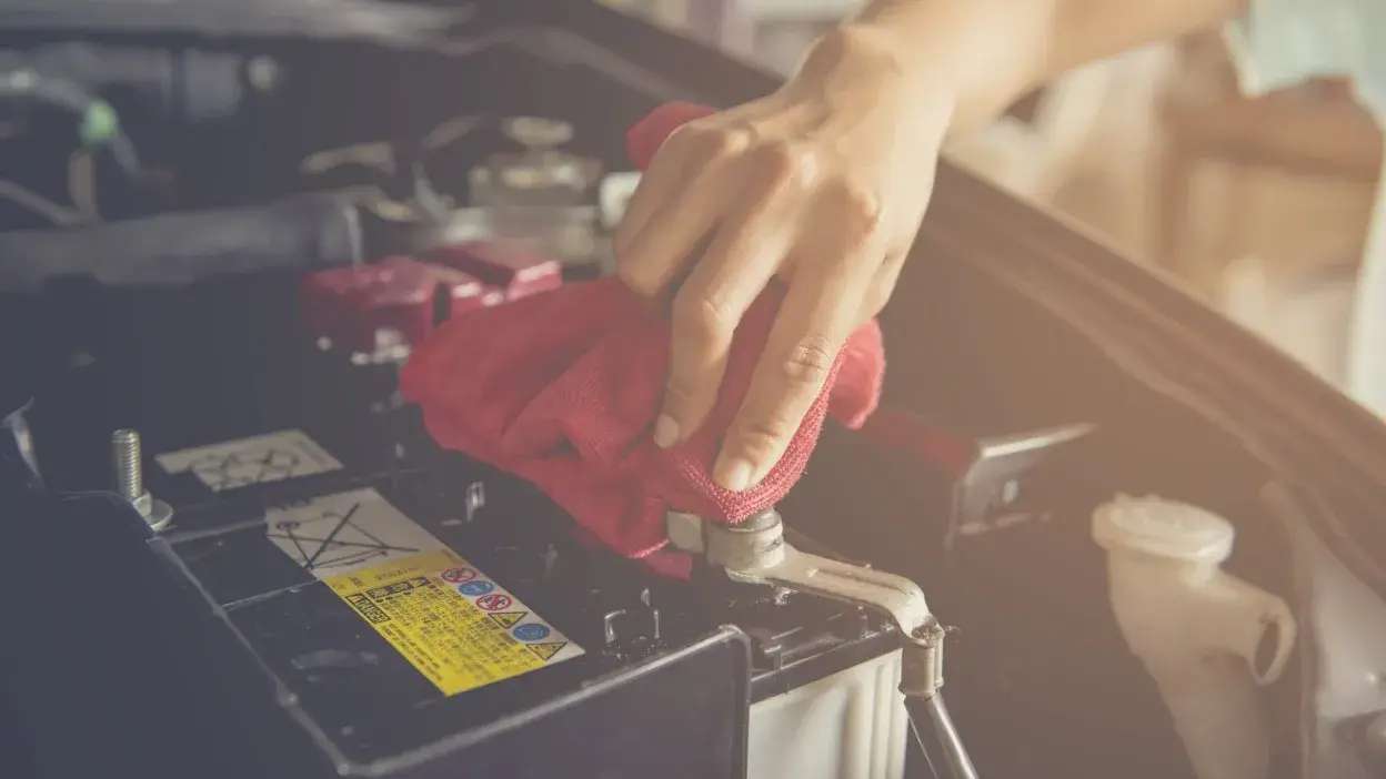 Mão a limpar o terminal de uma bateria de automóvel com um pano vermelho.