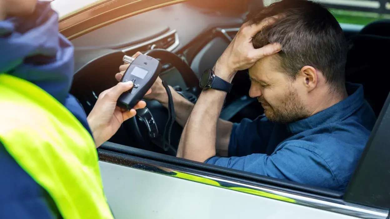 Homem no carro a ser submetido a teste de alcoolemia por agente da autoridade.