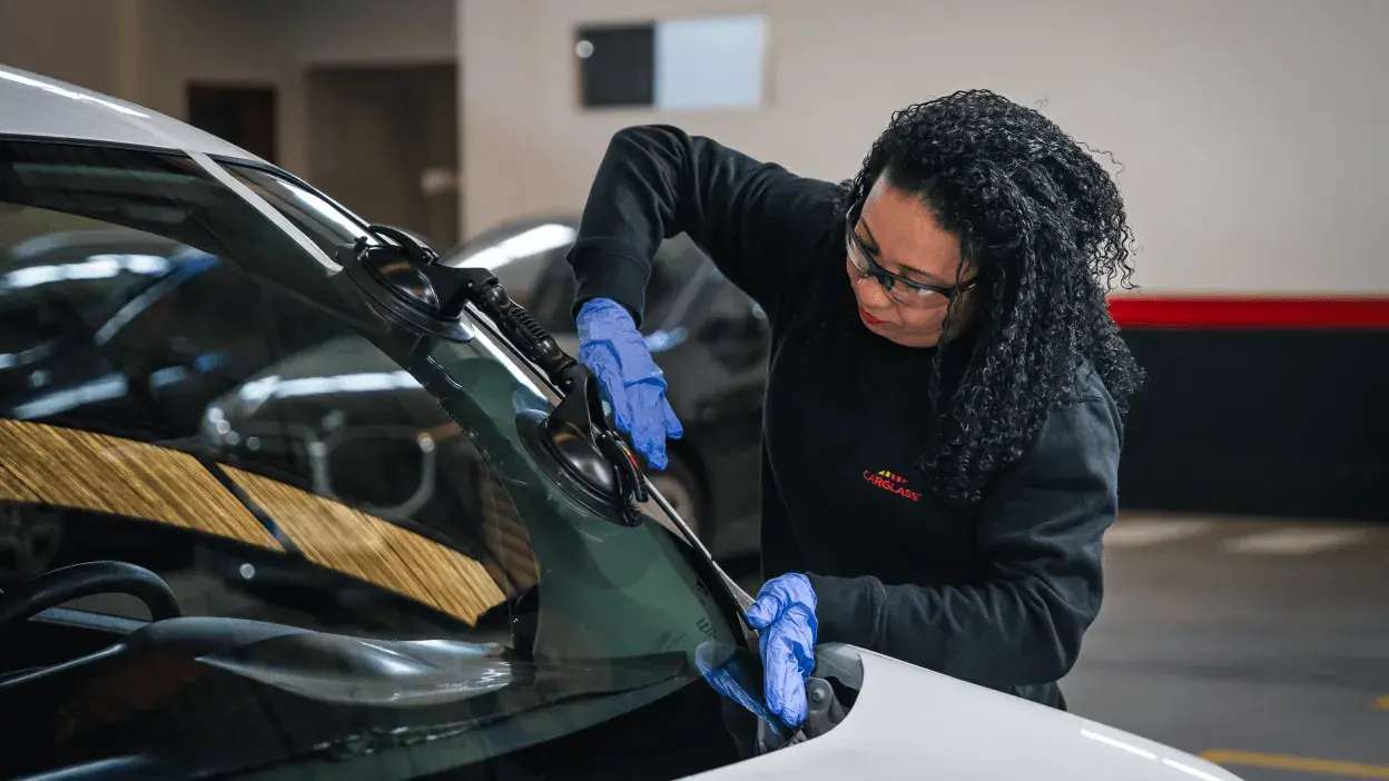 Técnica a instalar um para-brisas num carro com equipamento de sucção e luvas azuis.
