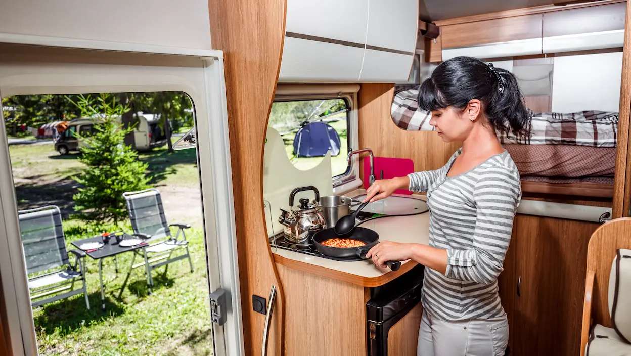 Mulher a cozinhar dentro de autocaravana em parque de campismo