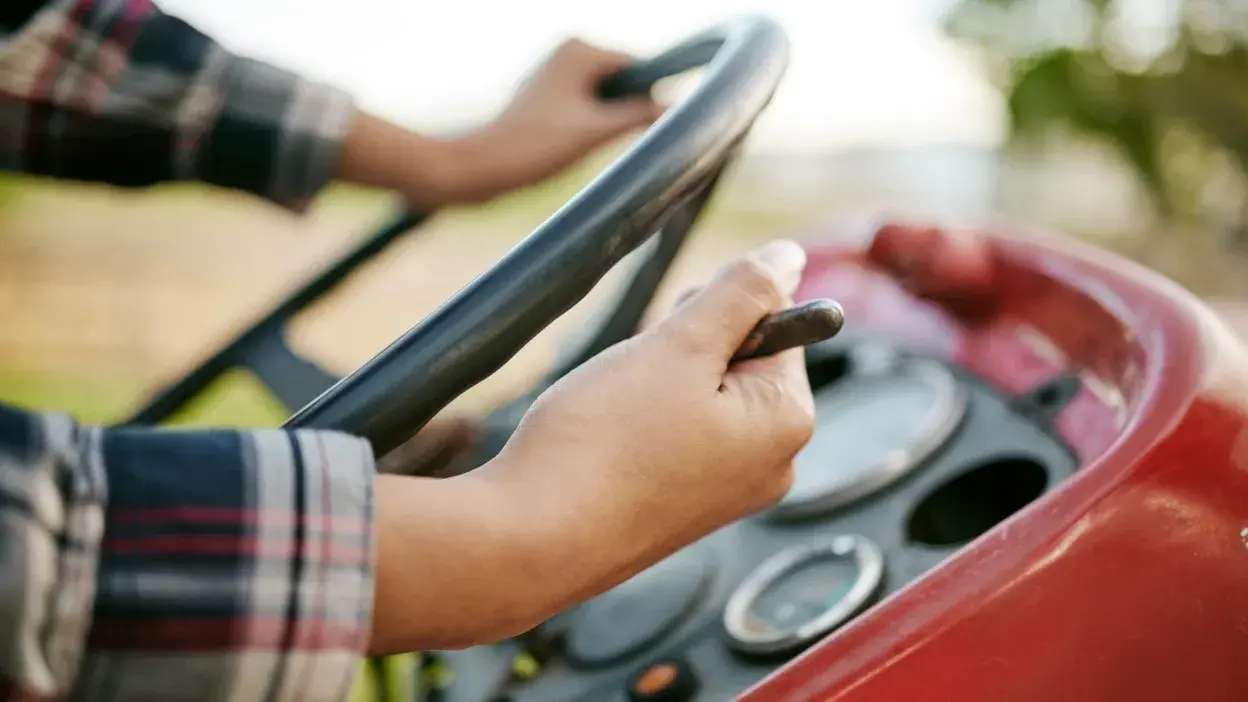 Mãos a conduzir um trator vermelho com volante e painel de instrumentos visíveis.