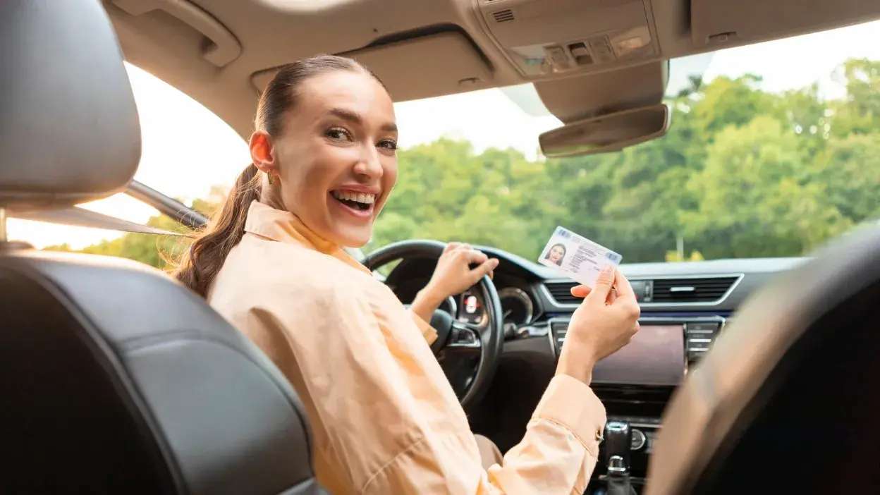 Mulher sorridente dentro de carro a mostrar uma carta de condução.