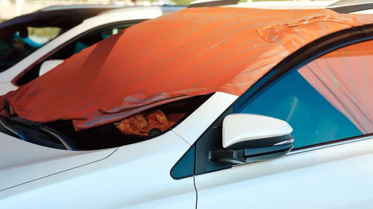 Cobertura laranja a proteger o para-brisas de um carro branco do sol
