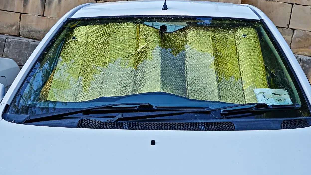 Protetor refletor colocado no interior do para-brisas de um carro branco para bloquear o sol.