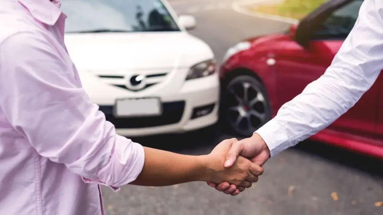 Duas pessoas a dar um aperto de mão perto de um acidente entre dois carros