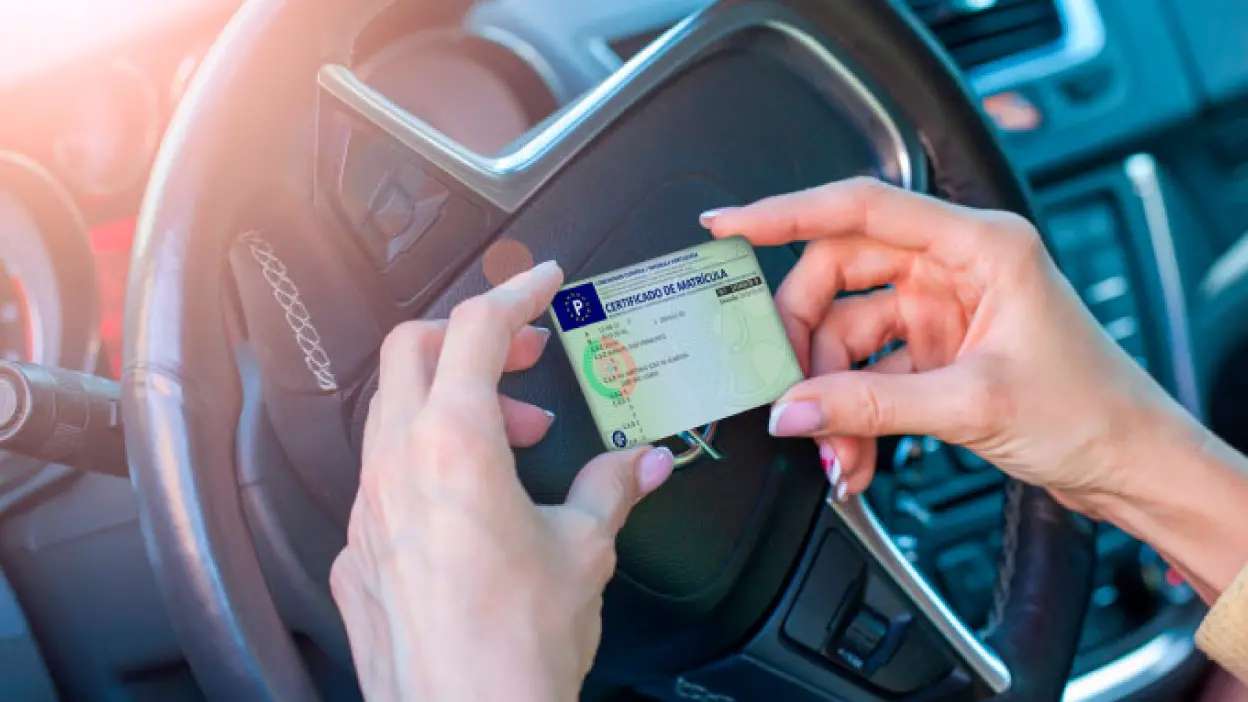 Pessoa ao volante de carro a segurar o documento único automóvel