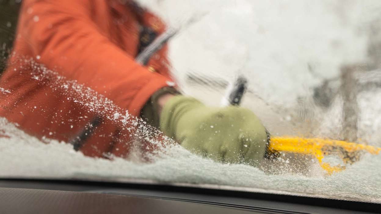 Senhora a raspar o gelo do para-brisas do carro com raspador de gelo amarelo