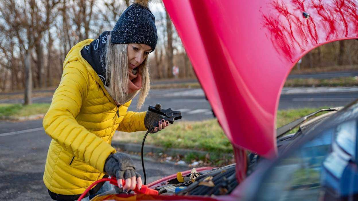 Senhora a ligar cabos à bateria do seu carro 
