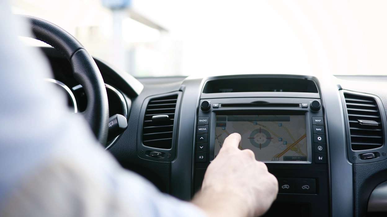 Senhor dentro do carro no lugar do condutor a mexer no ecrã e a ver trajeto