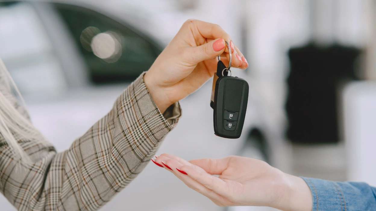 mão de mulher a segurar chave do carro e a entregá-la a outra pessoa com a mão estendida para receber a chave
