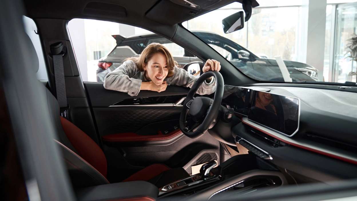 mulher a olhar para interior de carro novo, no stand, antes de o comprar