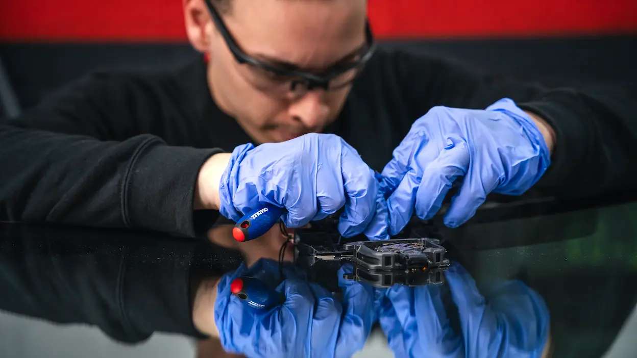 técnico da carglass, com luvas, a repara vidro para brisas de um carro