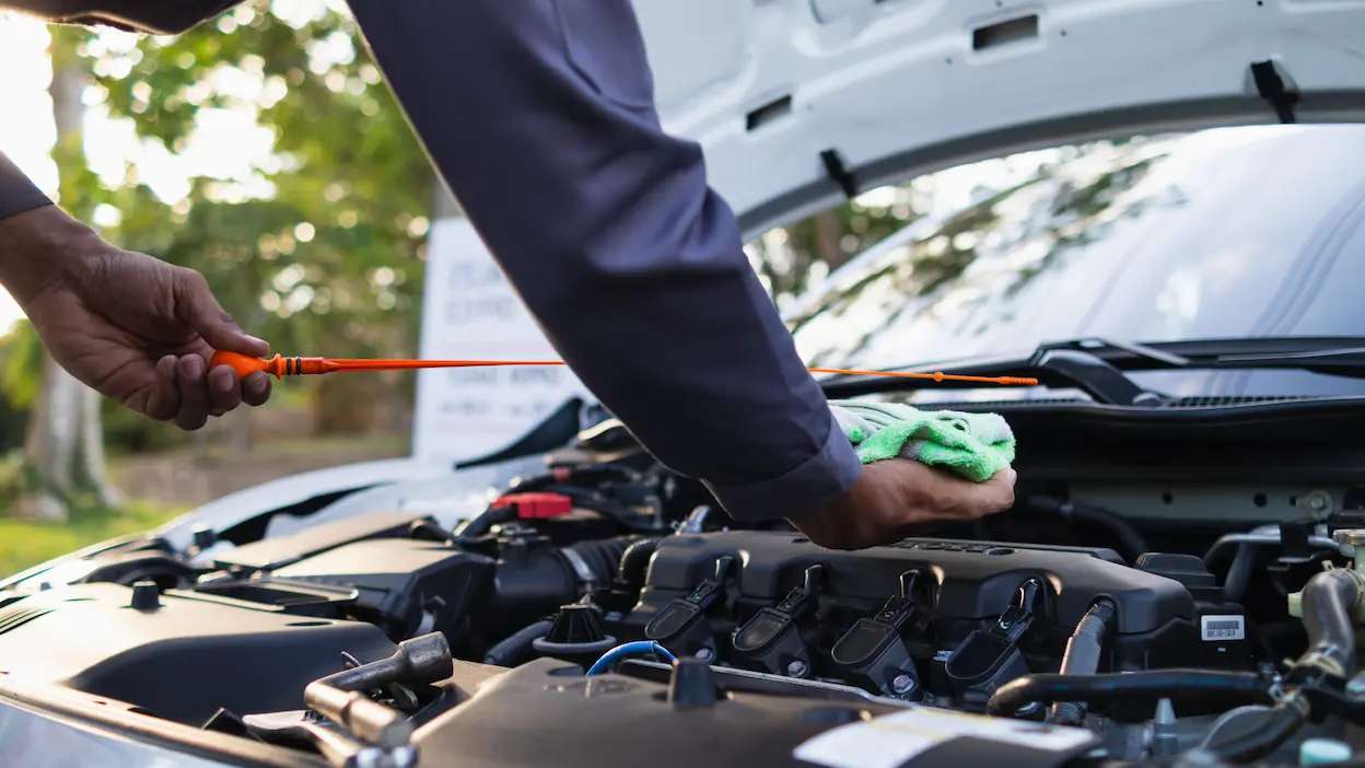 mecânico a verificar o óleo do carro, com vareta na mão e pano