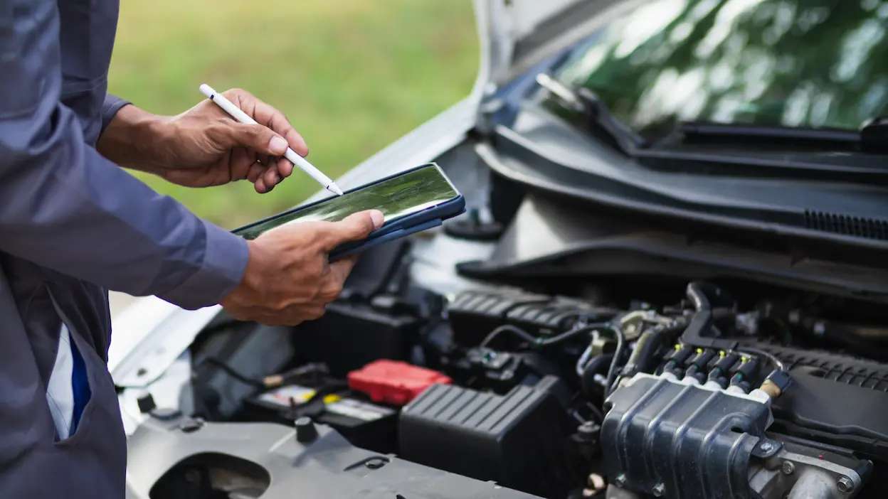 mecânico a fazer inspeção ao carro com o capot aberto e tablet na mão