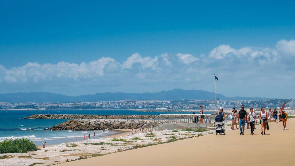 pessoas a passear no paredão das praias da costa da caparica