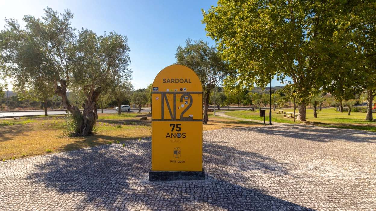 Monumento comemorativo da Estrada Nacional 2 em Sardoal, inserido numa zona verde com árvores e percurso pedonal