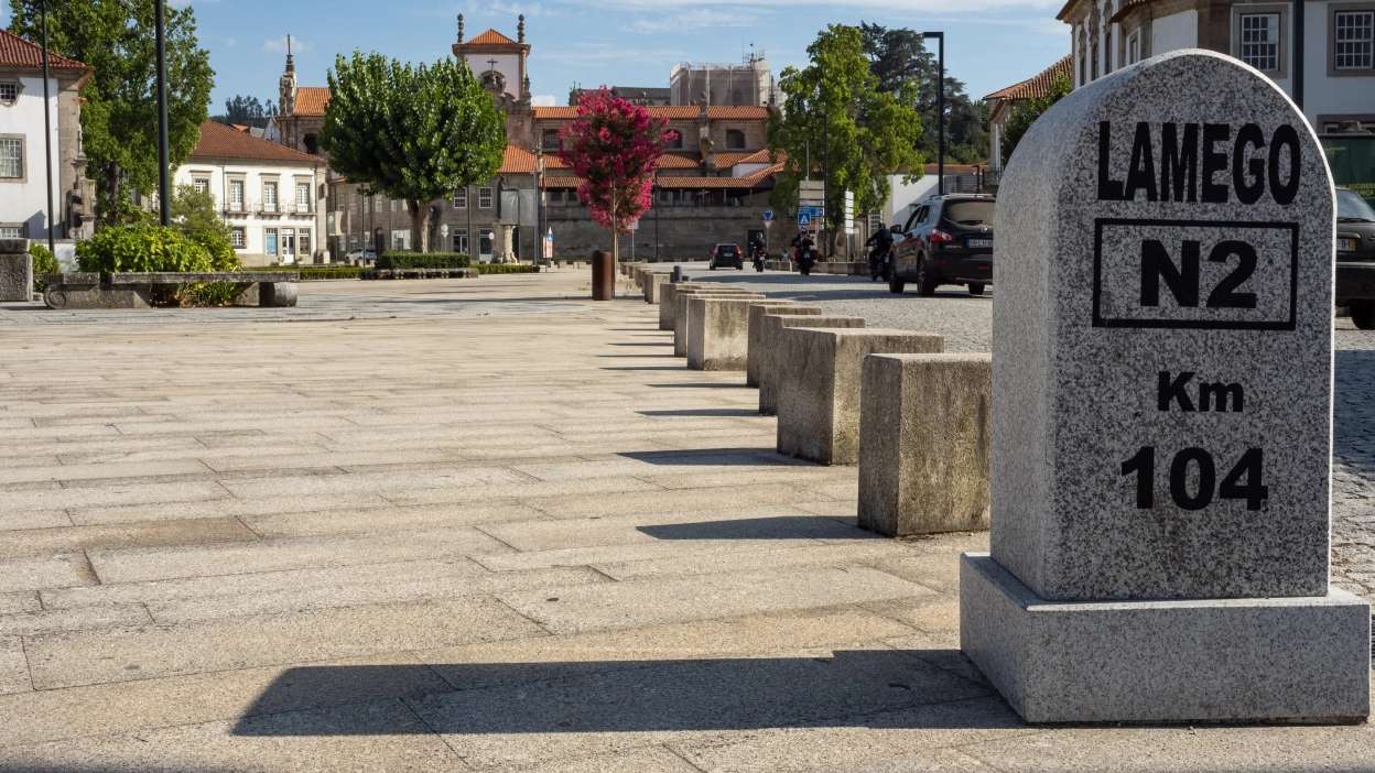 Marco quilométrico da Estrada Nacional 2 em Lamego, com vista para a praça e edifícios históricos da cidade
