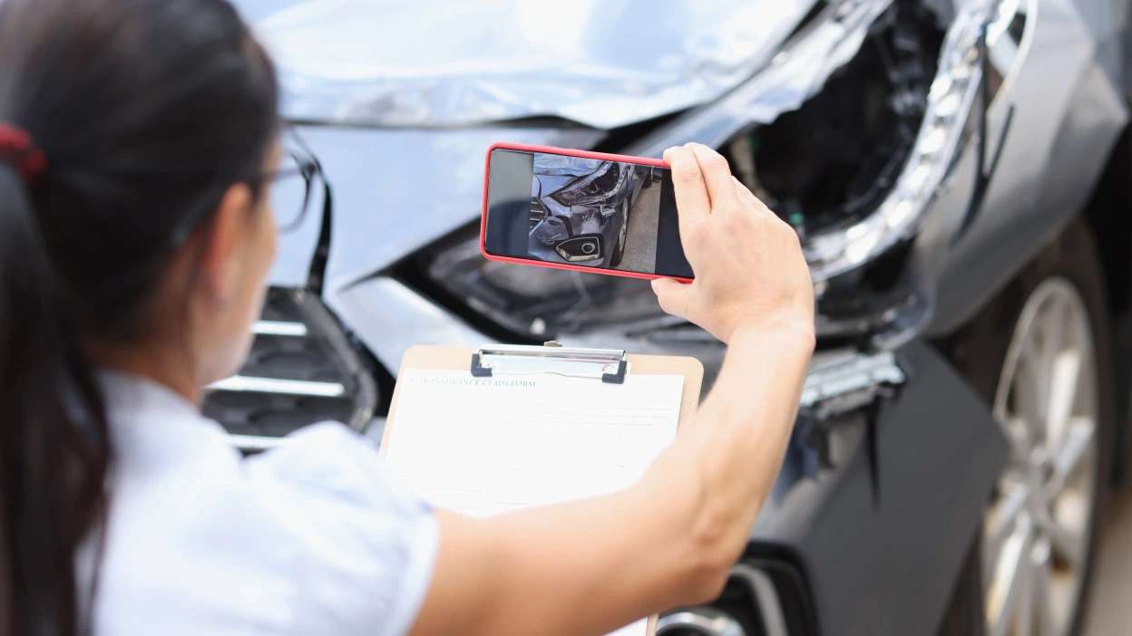 Pessoa a fotografar os danos na frente de um automóvel acidentado para avaliação ou participação de sinistro